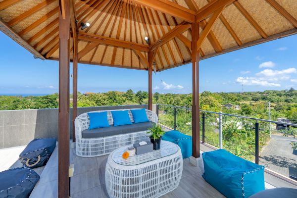 Spacious Balinese terrace pavilion with white rattan sofa, blue cushions, coffee table, and ocean horizon view. - Bali Villas